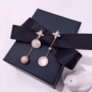 Detailed view of asymmetric rose gold earrings with shells, zircons and pink pearl on a gift box