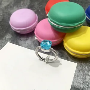 Anillo de cristal azul cuadrado con banda de diamantes sobre fondo de macarons