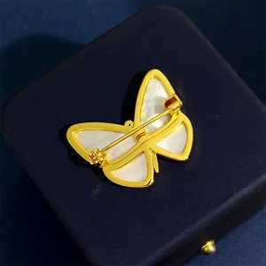 Elegant butterfly brooch with white shell in gold frame on a blue jewelry box