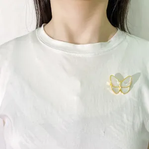 Elegant gold butterfly brooch with white shell wings on a white shirt pocket