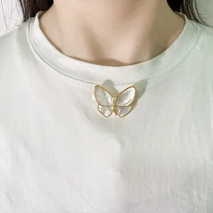 Detailed view of the butterfly brooch featuring white shell wings on a casual white shirt