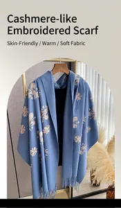 Detalle del chal de cachemira azul Morandi con bordado de flor de lis beige y flecos suaves