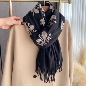 Primer plano de bufanda boho negra con bordado floral beige y detalles de flecos