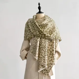 Détail d'une écharpe léopard vert mousse avec franges sur un manteau beige élégant