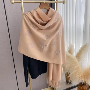 Elegante chal beige tipo cachemira con bordado floral y borlas en percha dorada