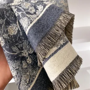 Deep blue and cream floral jacquard scarf with decorative fringe in a handheld close-up