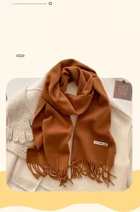 Detail of caramel cashmere-feel scarf with tassels and 10% wool label shown with autumn coat