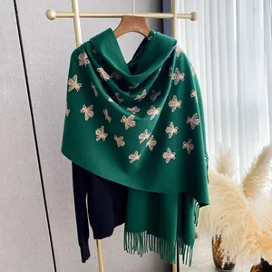 Detail of dark green cashmere-style shawl featuring gold bee embroidery and long tassels