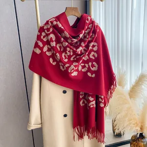 Dettaglio dello scialle rosso con ricamo leopardato e frange su un cappotto beige