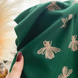 Macro shot of detailed bee embroidery on high-quality dark green cashmere-like scarf