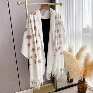 Detail of embroidered bee patterns and fine fringe on a white cashmere-feel shawl