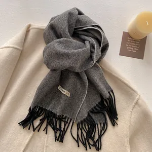Detail view of a 100% pure wool gray scarf with black tassels on a beige coat