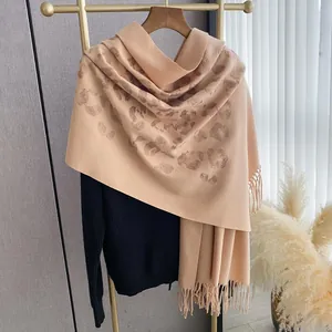 Dettaglio ricamo leopardato su sciarpa con frange appesa a una gruccia di legno chic