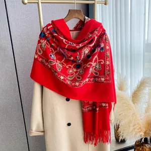 Thick red pashmina shawl with floral embroidery and tassels on a beige coat display
