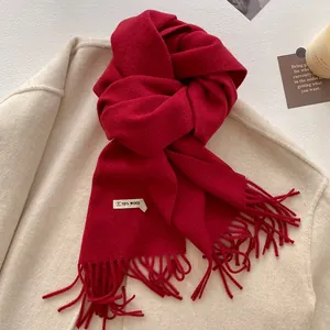 Close-up of thick red scarf with long tassels and wool blend texture over beige coat