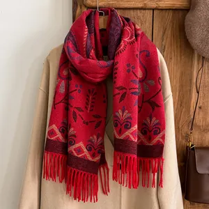 Detail of red jacquard scarf with floral patterns and tassels over a wool coat