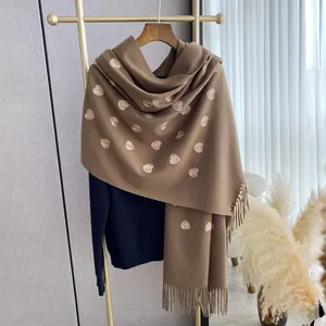 Dettaglio di sciarpa in cashmere cammello con ricamo a cuore dorato e frange