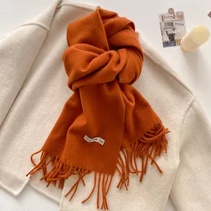 Detailed view of burnt orange wool scarf with thick fringe and 100% wool label