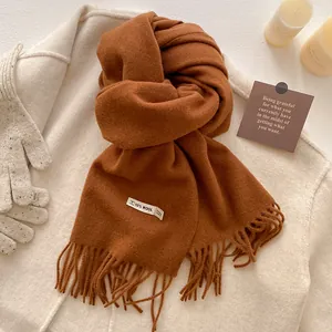Detailed close-up of a caramel brown wool blend scarf with elegant fringe trim and tag