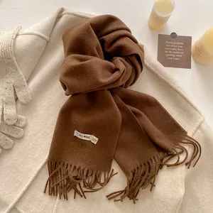 Detail view of brown tassel scarf with wool blend fabric and product label on beige coat