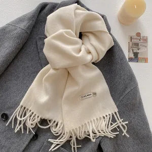 Detail of cream cashmere-feel scarf showing 10% wool label and fringe on grey coat