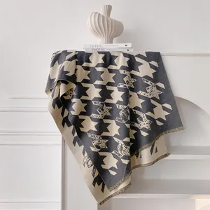 Detail of grey houndstooth shawl with fringe tassels hanging on a white minimalist shelf