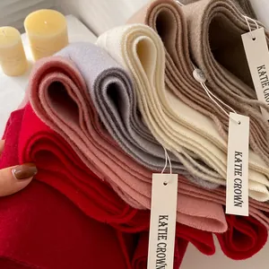 Thick cashmere-like scarves in various solid colors stacked on a white table with a candle