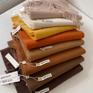 Solid color wool blend scarves with tassels in beige and earth tones stacked on white surface