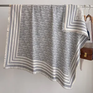 Detail eines eleganten grau-beigen Jacquard-Schals mit Buchstabenmuster und Fransen