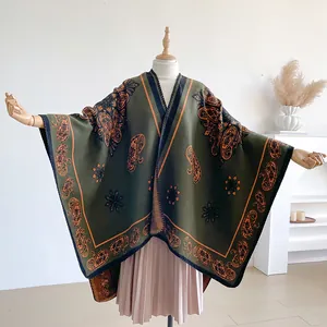 Detail of dark green knit poncho showing orange paisley patterns and fine edge stitching