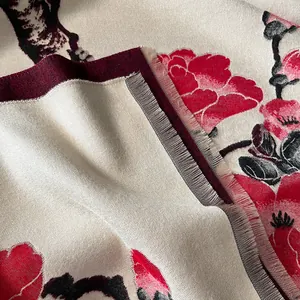 Close-up of red floral jacquard on thick white winter scarf with soft fringe detail