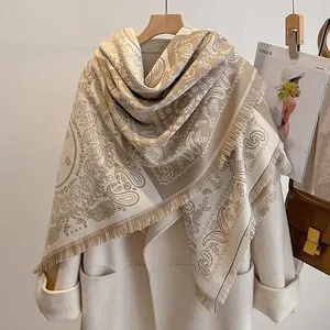 Détail du motif paisley et des franges sur l'écharpe en cachemire beige sur manteau blanc