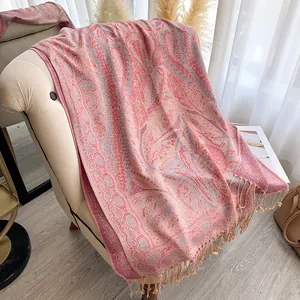 Détail d'un châle jacquard à motif paisley rose avec franges sur un fauteuil beige