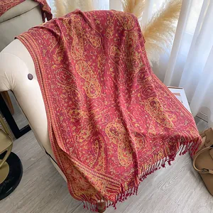 Detail van rode paisley sjaal met gouden patronen en franjes op de fauteuil
