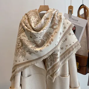 Détail d'un châle beige effet cachemire avec motifs jacquard licorne et étoile à franges