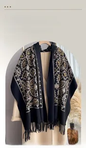 Detailed embroidery and tassel on black cashmere-feel scarf draped over a coat