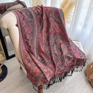 Détail macro d'une écharpe en cachemire rouge à motifs paisley avec des pompons noirs