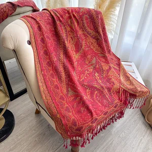 Détail d'un châle cachemire rouge à motifs paisley dorés et pompons sur un fauteuil