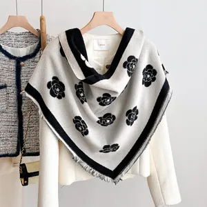 Detail of cream knit shawl featuring black camellia floral patterns and fringed edges