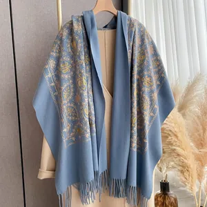 Detail of light blue faux cashmere shawl featuring golden paisley embroidery and tassel trim