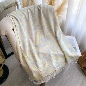 Detail of paisley pattern long shawl with tassels draped over a soft fabric sofa