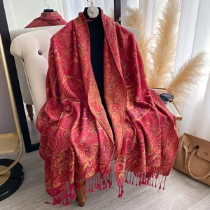 Red paisley jacquard shawl with fringe hanging in a warm and minimalist indoor setting