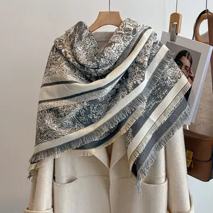 Détail d'une écharpe grise à motifs vintage et franges longues sur un manteau beige