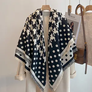 Détail d'écharpe pied-de-poule noire et blanche à pois avec franges sur manteau beige