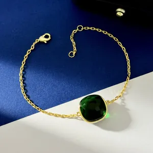 Close-up of a gold alloy bracelet featuring a faceted square green crystal and lobster clasp