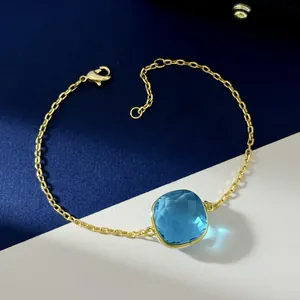 Macro detail of gold-plated bracelet with sky blue cushion-cut crystal and lobster clasp