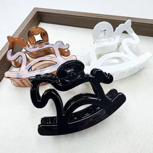 Modern horse-shaped hair claws in black, white, and amber colors on a grey background