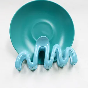 Vista macro del fermaglio per capelli ondulato azzurro con finitura lucida su piatto verde