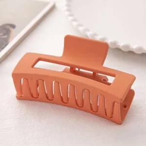 Grosse pince à cheveux orange mat en acrylique sur un fond texturé blanc élégant
