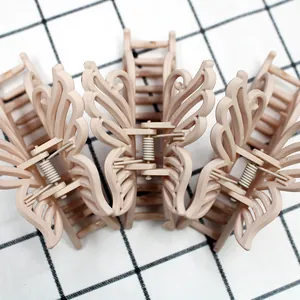 Three large matte butterfly hair claws in beige color placed on a checkered fabric background